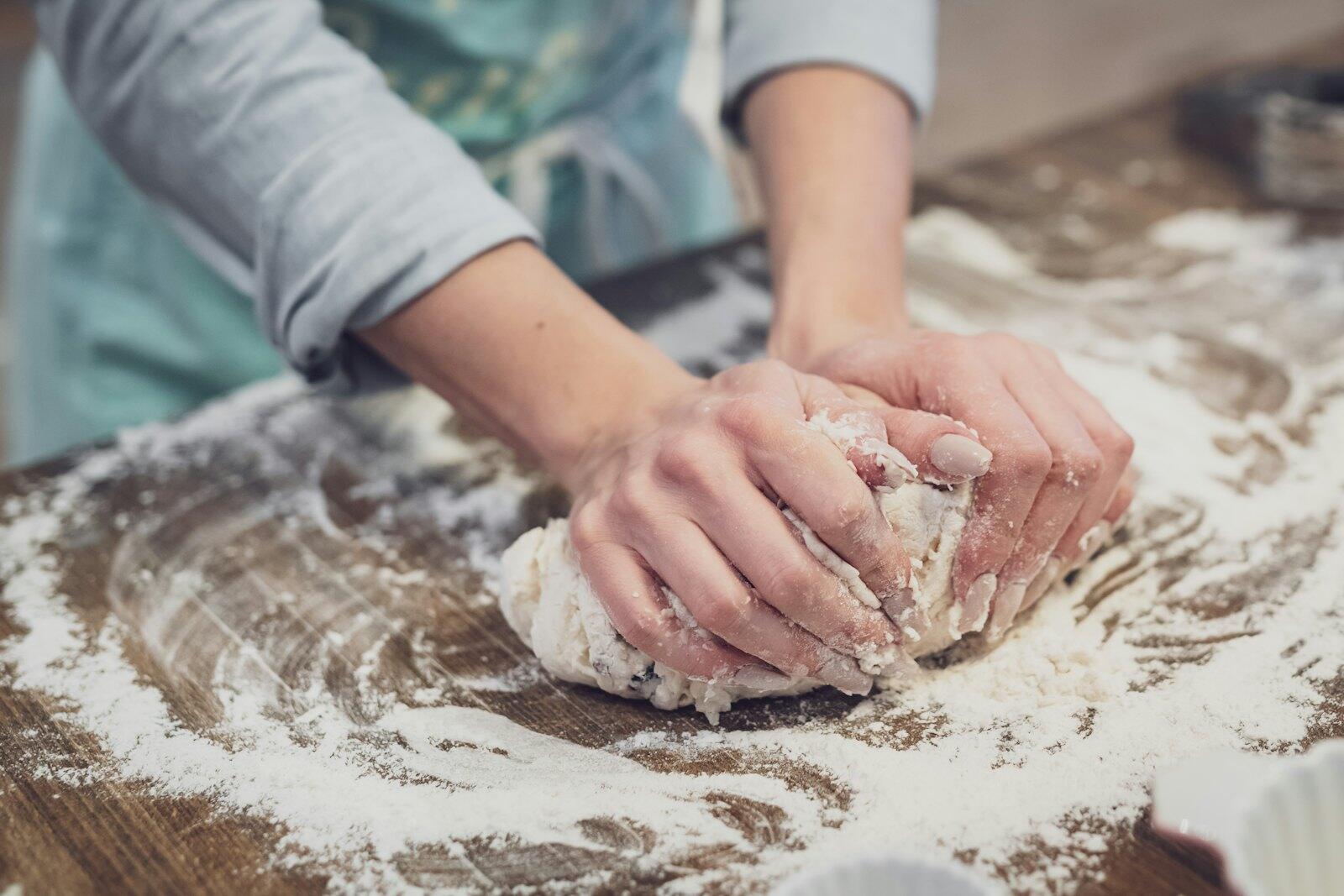 Mains qui pétrissent une pâte sur un plan fariné
